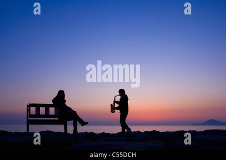 Guy à jouer du saxophone pour la femme sur la plage Banque D'Images