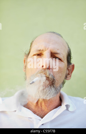 Portrait of mature white man looking at camera contre mur vert avec la cigarette dans la bouche. Copy space Banque D'Images