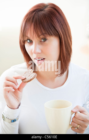 Attractive young woman eating a biscuit chocolat et de boire une tasse de café Banque D'Images