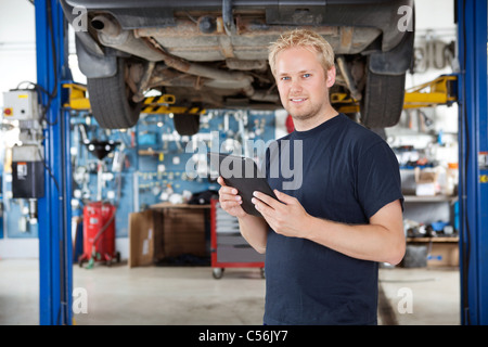 Portrait of young mechanic holding digital tablet dans son atelier de réparation automobile Banque D'Images
