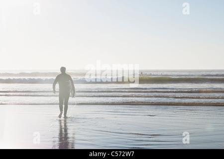 Surfer carrying surfboard hors de l'eau Banque D'Images