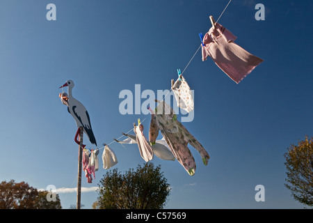 Les Pays-Bas, Lattrop, Stork en bois avec baby doll, pour montrer qu'un bébé est né. Vêtements de bébé sur corde à linge. Banque D'Images