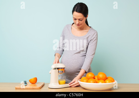 Photo d'une femme enceinte de la semaine 32 dans sa cuisine préparer le jus d'orange fraîchement pressé. Banque D'Images