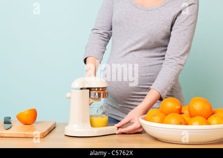 Photo d'une femme enceinte de la semaine 32 dans sa cuisine préparer le jus d'orange fraîchement pressé. Banque D'Images