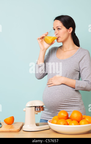 Photo d'une femme enceinte de la semaine 32 dans sa cuisine de boire du jus d'orange fraîchement pressé. Banque D'Images