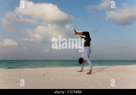 Businessman doing handstand on beach Banque D'Images