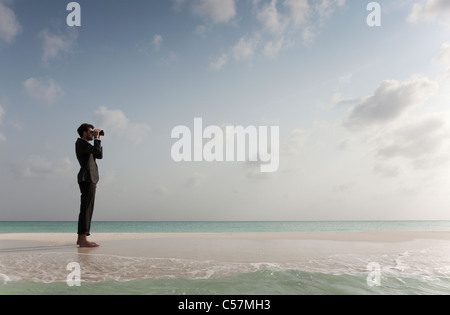 Businessman using binoculars on beach Banque D'Images