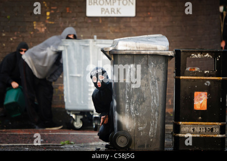 Porter des émeutiers balaclava avec initiales FTPSNI' se cache derrière une poubelle avec une pierre dans sa main à jeter sur la police. Deux émeutiers derrière transporter une caisse de cocktails molotov à jeter Banque D'Images