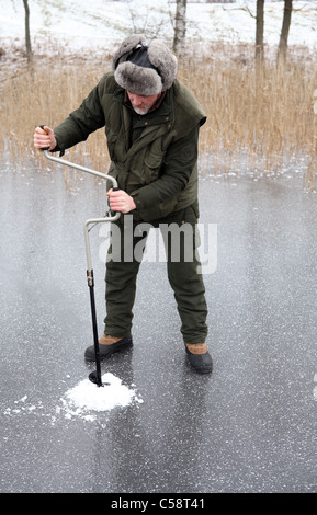 Un homme pêche sur glace le forage d'un trou dans le lac Stora Bellen, Belloe, Suède Banque D'Images