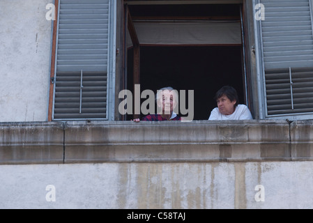 Une vieille femme italienne Senior citizen et son gardien femelle regarder par une fenêtre du troisième étage à Florence, Italie. Banque D'Images