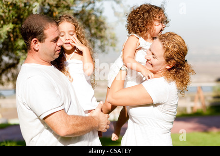 Maman et papa avec leurs enfants dans le parc, maman essaie de mettre son enfant sur ses épaules Banque D'Images