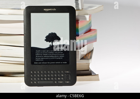 Amazon Kindle e-reader à côté d'un tas désordonné de livres traditionnels et un fond uni. Banque D'Images
