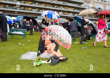 Une femme était assise sur l'herbe à côté de deux bouteilles de vin blanc reste sec sous un parapluie sous la pluie à Royal Ascot. Banque D'Images