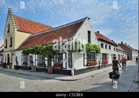 Les cyclistes faire du vélo le long des restaurants et des maisons blanches typiques au petit village Lissewege en Flandre occidentale, Belgique Banque D'Images