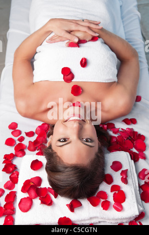 Smiling belle femme allongée sur une table de massage avec des pétales de rose autour de