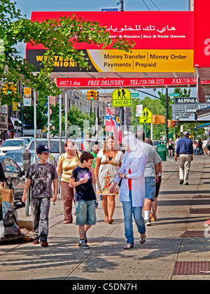 Une adolescente musulmane dans un foulard passe un bilingue français/arabe street sign dans la 'Petite Beyrouth" à Brooklyn, New York. Banque D'Images