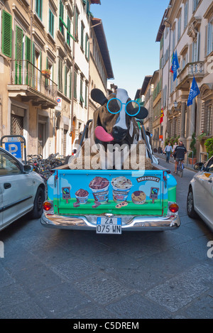 Une vache noir et blanc sculpture se dresse à l'arrière d'un camion avec des balles de foin, cerclée de bleu et rose lumineux lunettes de langue maternelle. Banque D'Images