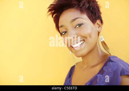 Magnifique africaine college student smiling and looking at camera contre mur jaune. copy space Banque D'Images