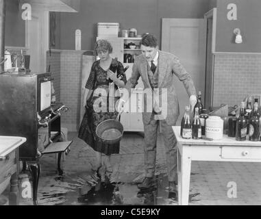 L'homme et la femme regardant le liquide répandu sur le sol de la cuisine Banque D'Images