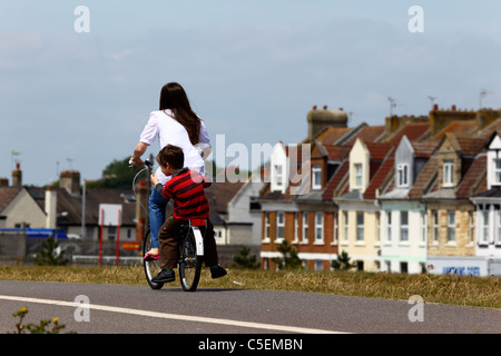 Femme et enfant en vélo le long de la rue housing estate, St Leonards on Sea, East Sussex, Angleterre Banque D'Images