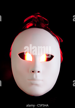 Effrayant masque blanc aux yeux rouges sur fond sombre Banque D'Images