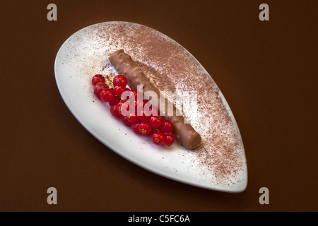 Une praline au chocolat sur une plaque blanche avec la poudre de cacao et de groseille rouge Banque D'Images