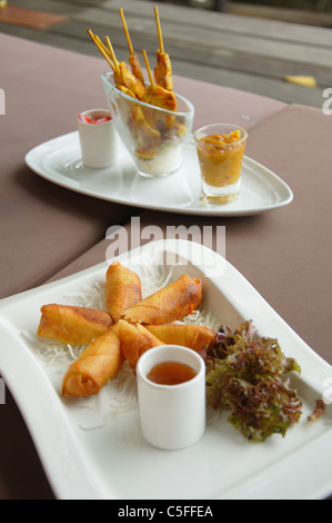 Des rouleaux de printemps sur une plaque avec un poulet satay plaque dans l'arrière-plan sur un resort à Lamay, Koh Samui en Thailande Banque D'Images