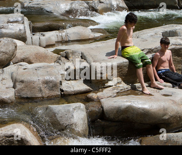 Deux jeunes garçons assis sur de grosses roches à un trou de natation. Banque D'Images