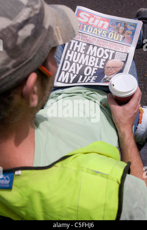 Un ouvrier se lit une copie du journal Sun tabloïd publié par Rupert Murdoch's News International. Banque D'Images