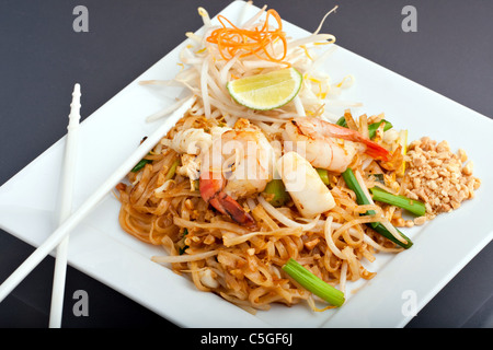 Pad Thaï de fruits de mer plat de nouilles de riz frit thaïlandais sur place une plaque blanche avec des baguettes et de carotte râpée garniture. Banque D'Images