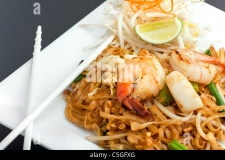 Pad Thaï de fruits de mer plat de nouilles de riz frits sur une plaque carrée blanche avec des baguettes et de carotte râpée garniture. Banque D'Images