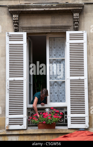 Femme participant à géraniums dans la fenêtre à volets dans le vieux Bergerac Dordogne Aquitaine France Banque D'Images