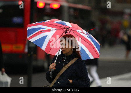 Une femme en attente de traverser une route et s'abritant sous son parapluie dans une douche de pluie Banque D'Images