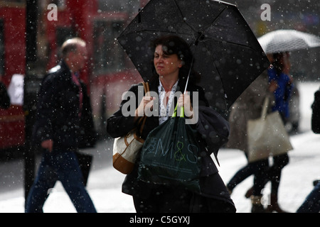 Une dame en attente de traverser une route et s'abritant sous son parapluie dans une douche de pluie Banque D'Images