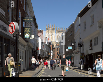 Magasins du centre-ville magasins en été et West Towers of the Minster en arrière-plan Low Petergate York North Yorkshire Angleterre Royaume-Uni Banque D'Images