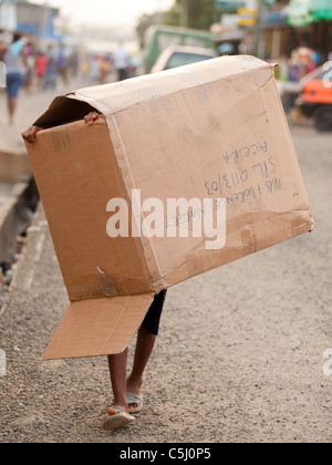 Garçon marchant le long d'une rue portant une grande boîte en carton sur sa tête à Osu, Accra, Ghana. Banque D'Images