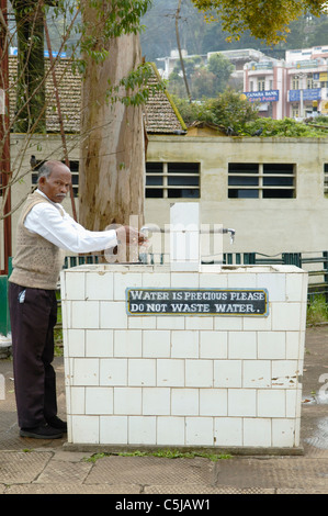 L'homme indien à l'aide d'un distributeur d'eau publique à Coonoor railway station, Coonoor. L'Inde, le Tamil Nadu, Ooty, 2005. Banque D'Images