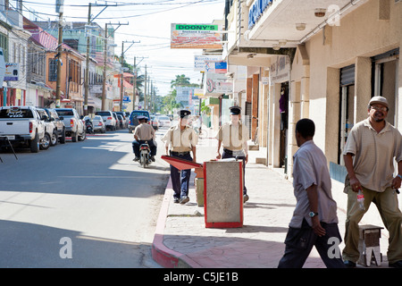 Deux agents de police walking on sidewalk tandis qu'un autre deux passe en scooter dans le centre-ville de Belize City, Belize Banque D'Images