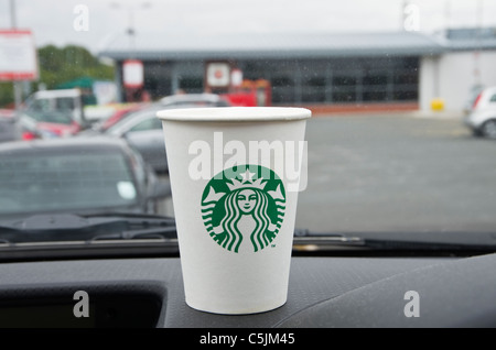 Le Starbucks café à emporter pour aller dans une tasse de papier à emporter-go avec nouveau logo sur un tableau de bord de voiture dans une station-service sur autoroute. Angleterre, Royaume-Uni Banque D'Images