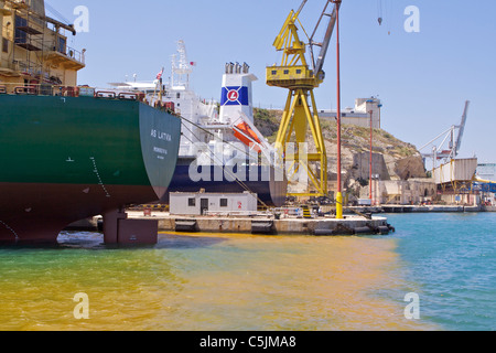 Grandes grues de chargement et des remontées mécaniques dans le Grand Port de La Valette avec du jaune de l'eau polluée Banque D'Images