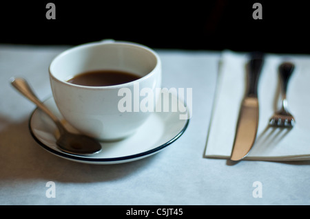 Tasse de café, cuillère, fourchette, couteau et serviette dans un petit restaurant. Banque D'Images