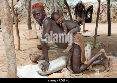 Portrait d'un tribeswoman Karo et son bébé moudre le grain au village de Kolcho dans la basse vallée de l'Omo, dans le sud de l'Éthiopie. Banque D'Images