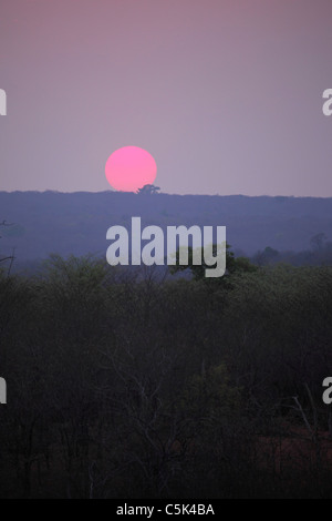 Coucher de soleil sur le Victoria Falls National Park, Zimbabwe. Le soleil est orange dans la brume jusqu'à tomber au-dessous de l'horizon. Banque D'Images