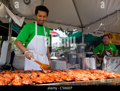Un homme asiatique assaisonnement s'applique sur les brochettes de poulet à l'aide d'un pinceau - USA Banque D'Images