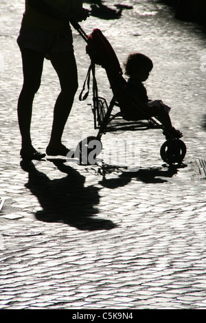 Femme de l'ombre des jambes pieds poussant dans la pram bébé soleil en rue en ville Banque D'Images