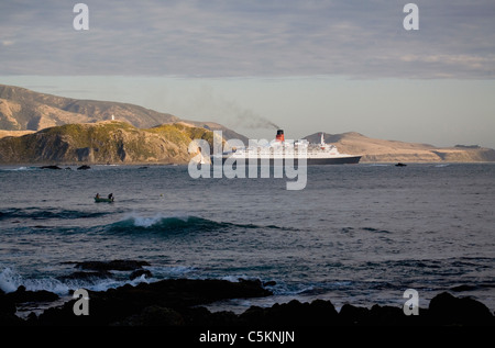 Un paquebot de croisière Queen Elizabeth 2 voile passé hills à l'entrée du port de Wellington, Nouvelle-Zélande, deux hommes d'une petite pêche Banque D'Images