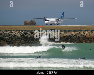 Un avion ATR-72 d'Air New Zealand sur la piste à l'Aéroport de Wellington avec surfers à Lyall Bay en premier plan Banque D'Images