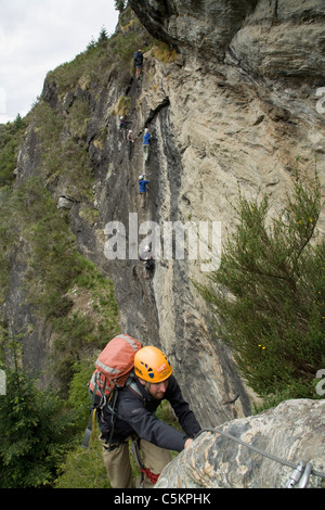L'homme de l'escalade avec 6 personnes l'ascension d'une falaise face à l'arrière-plan, Queenstown, Nouvelle-Zélande Banque D'Images