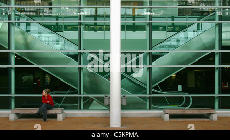 Deux escaliers escaliers mécaniques (déménagement) vu à travers la fenêtre de verre vert, une femme en rouge haut assise sur un banc à l'extérieur, Wellington Banque D'Images