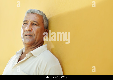 Portrait de 50 ans homme d'Amérique latine ayant des problèmes et s'appuyant sur mur jaune. De forme horizontale, copy space Banque D'Images